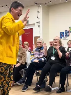 Sunny Turner leading a Laughter Yoga session with a group - participants laughing and clapping together